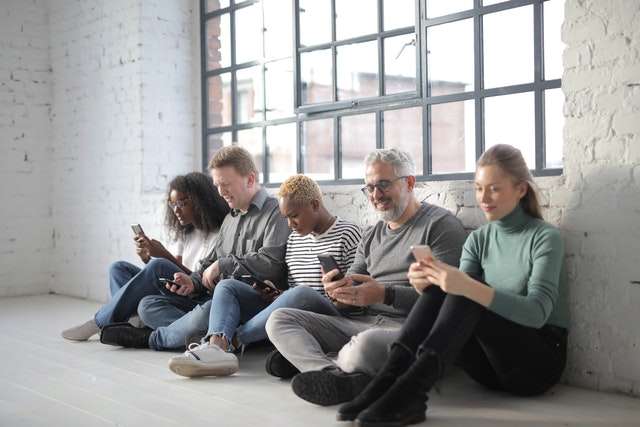 Group of mixed age and race people sitting against the wall with mobile devices