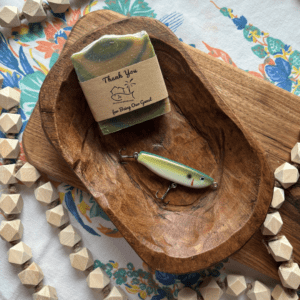 Flatlay photo of a bar of goat's milk soap and a handcrafted fishing lure