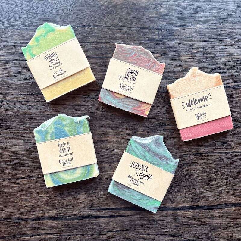Flatlay photo showing a collection of five guest soaps with fun welcoming labels on them for vacation rental guests