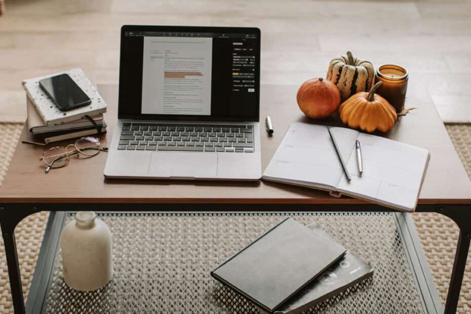 An open laptop, multiple notebooks and pen on top of a table.